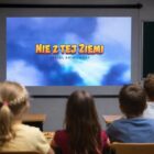 Dzieci w klasie oglądają serial Nie z Tej Ziemi wyświetlany na ekranie